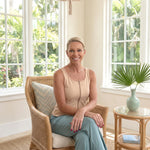 Woman sitting in a wicker chair in a bright room with large windows and plants. Woman is wearing a zipper front opening tank top 