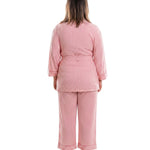 A woman viewed from the back wearing a pink vertically striped pajama set with a sash tie top and matching pants, standing against a plain white background.