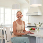 Woman wearing a beige zipper front opening tank top sitting at a kitchen counter with a bright and airy kitchen in the background