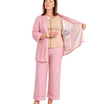 A woman wearing pink striped recovery  pajamas set with and a beige mastectomy tank top, holding open the striped top while demonstrating a clear plastic  tubing and surgical jp drain placement into the interior pocket.