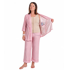A woman wearing pink striped recovery  pajamas set with and a beige mastectomy tank top, holding open the striped top while demonstrating a clear plastic  tubing and surgical jp drain placement into the interior pocket.