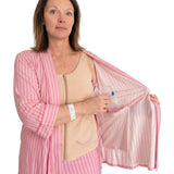 A woman wearing pink striped recovery  pajamas set with and a beige mastectomy tank top, holding open the striped top while demonstrating a clear plastic  tubing and surgical jp drain placement into the interior pocket.