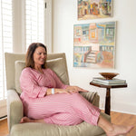 A woman wearing a vertically striped pajama robe top and matching pants sitting on a beige chair 