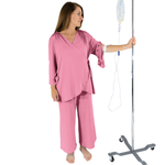 Woman in pink pajamas holding an IV stand on a white background