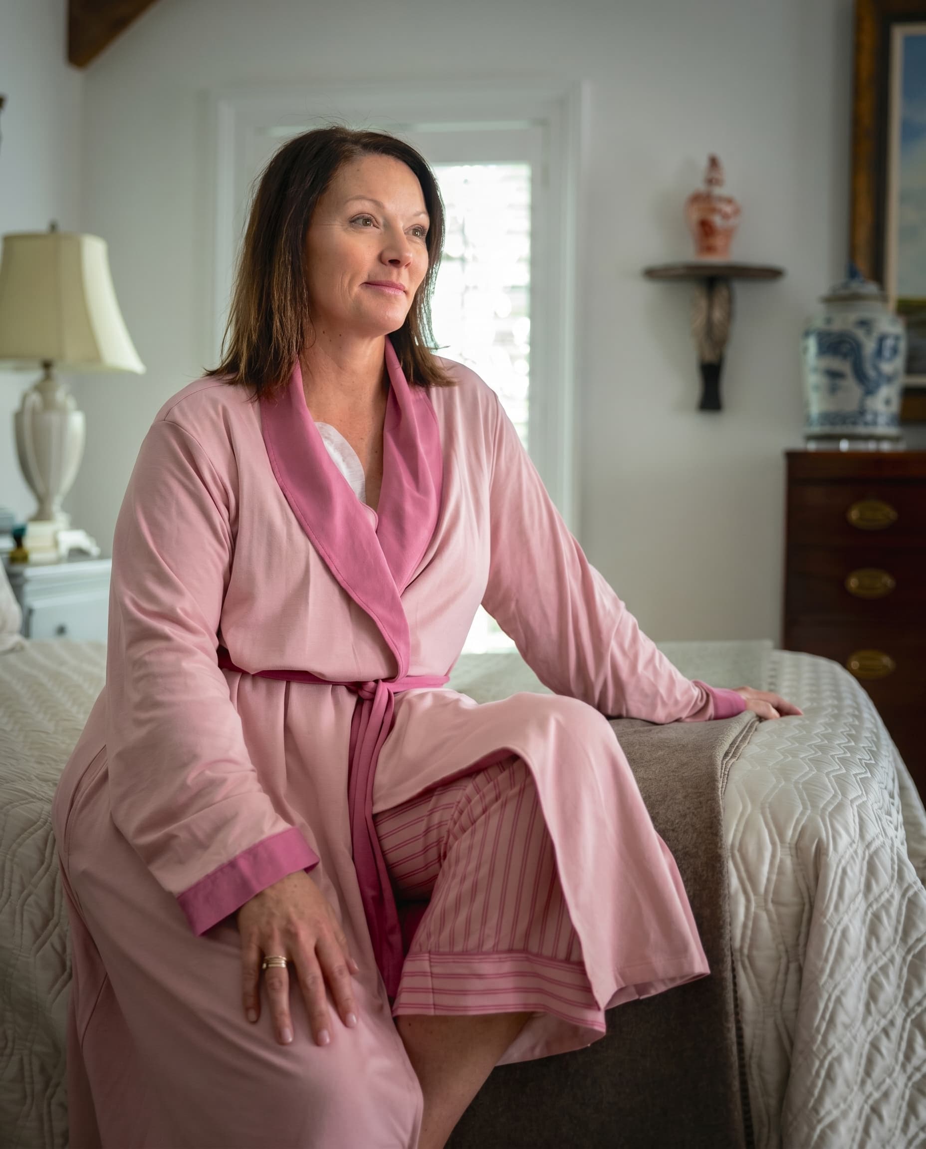 Woman in a pink recovery robe sitting on a bed in a bedroom.