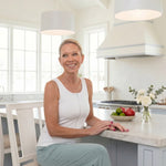 Woman wearing a white zipper front opening tank top sitting at a kitchen counter with a bright and airy kitchen setting