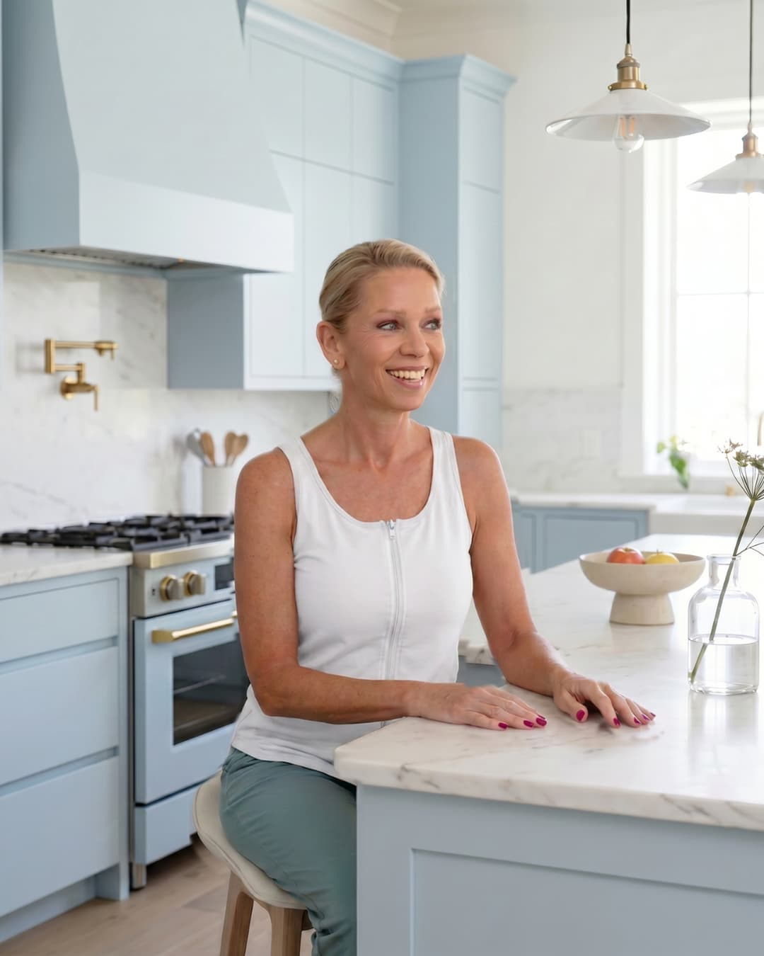 Woman wearing a white zipper front opening tank top sitting at a kitchen counter in a modern kitchen