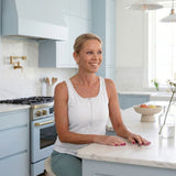 Woman wearing a white zipper front opening tank top sitting at a kitchen counter in a modern kitchen