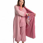 Woman wearing a pink recovery robe with an surgical bag going into the internal pocket on a white background