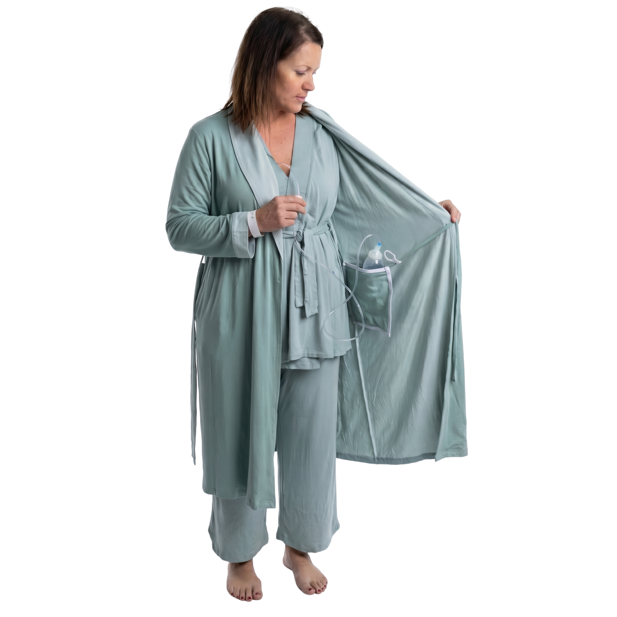 Woman wearing a sage green recovery robe with an surgical bag going into the internal pocket on a white background