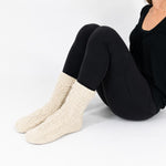 Person wearing oatmeal-beige cable knitted socks on a white background