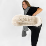 Person wearing oatmeal-beige cable knitted socks gripper bottoms for safety kicking their foot out so you see the grips, on a white background.