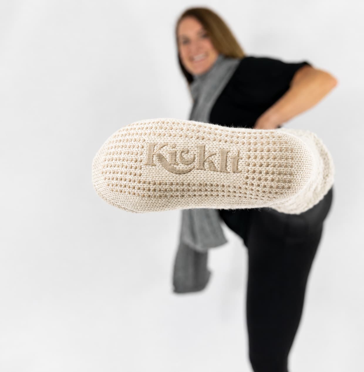 Person wearing oatmeal-beige cable knitted socks gripper bottoms for safety kicking their foot out so you see the grips, on a white background.