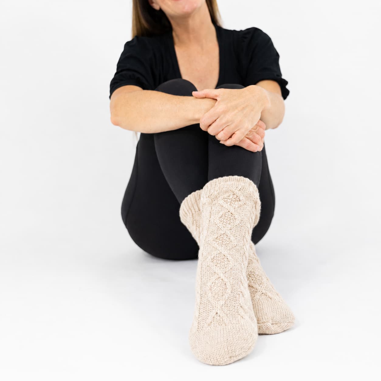 Person wearing oatmeal-beige cable knitted socks on a white background