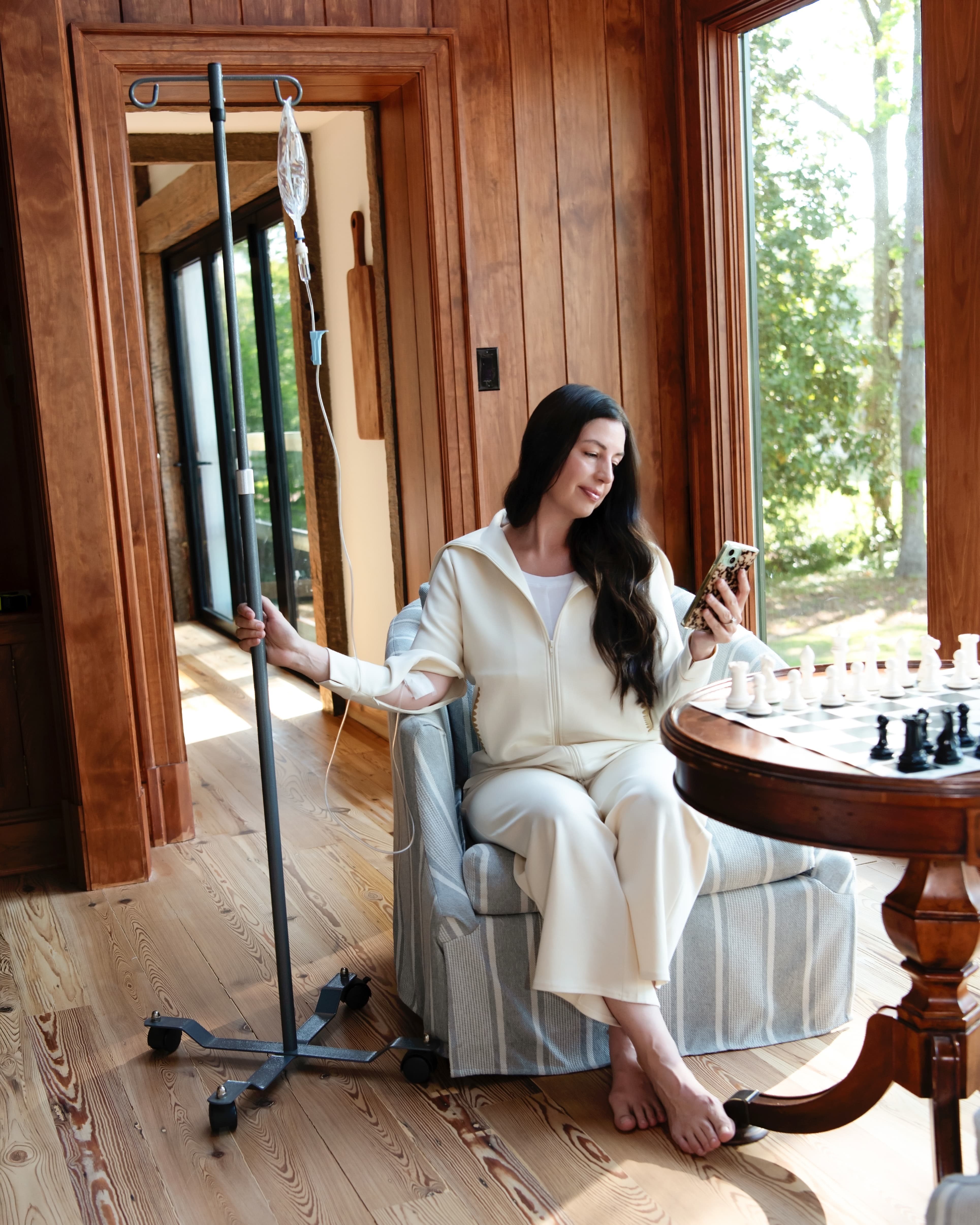 Woman sitting in a chair with an IV stand next to her, holding a phone.