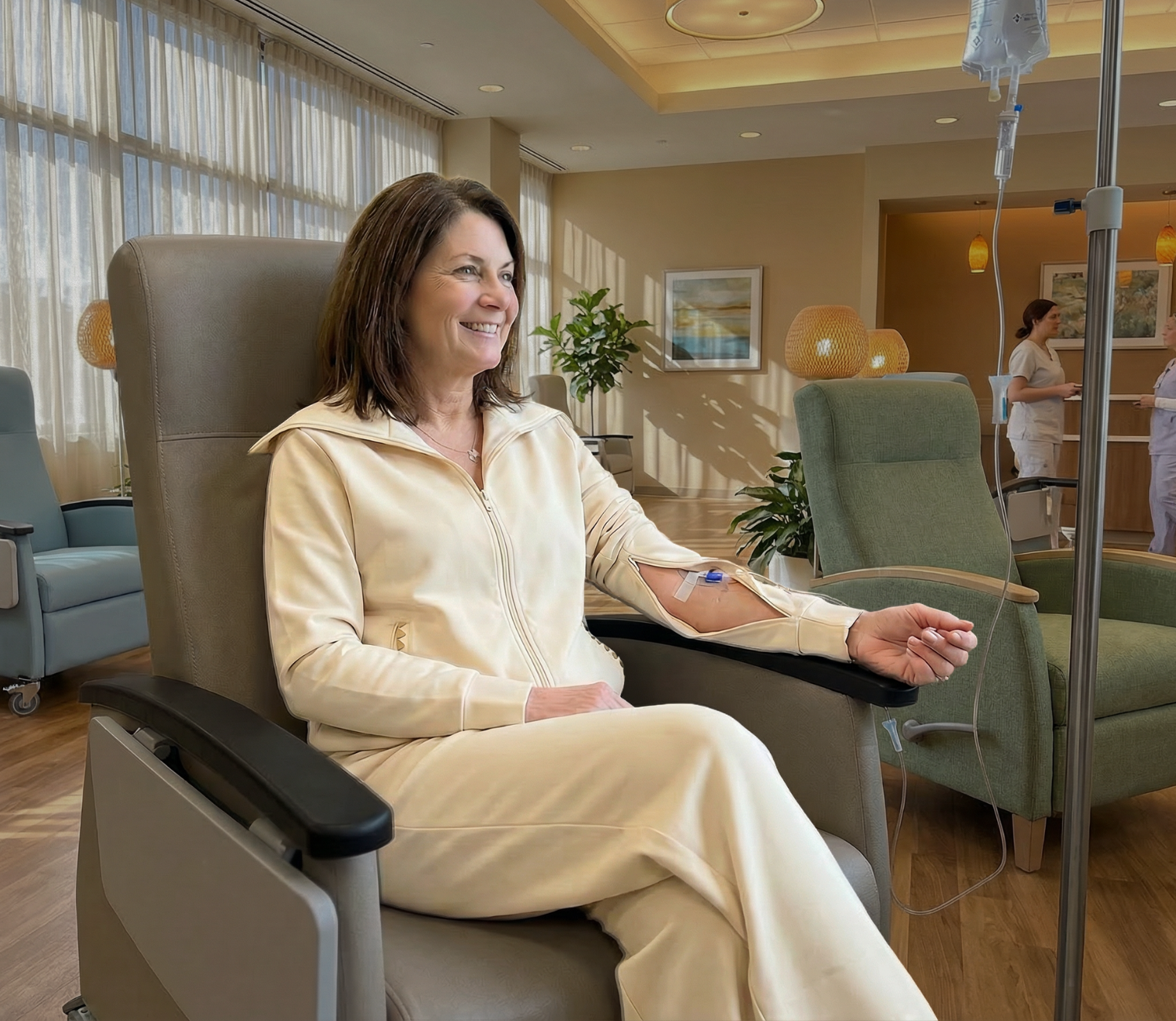 Woman receiving an intravenous treatment in a hospital room in a cream colored loungewear set with arm zippers for medical access
