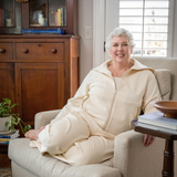 Woman sitting on a couch wearing a cream-colored recovery set, in a cozy living room setting.
