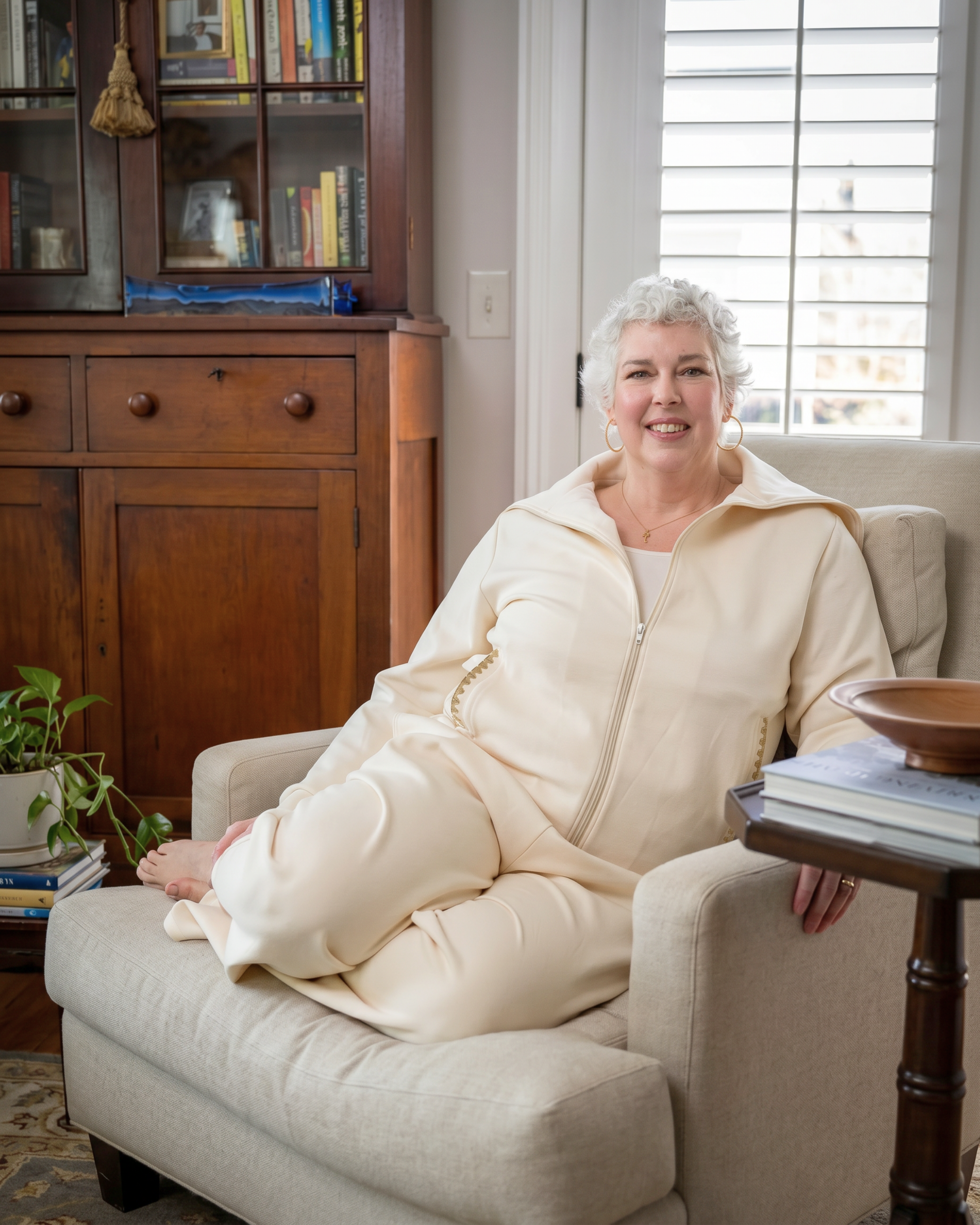 Woman sitting on a couch wearing a cream-colored recovery set, in a cozy living room setting.
