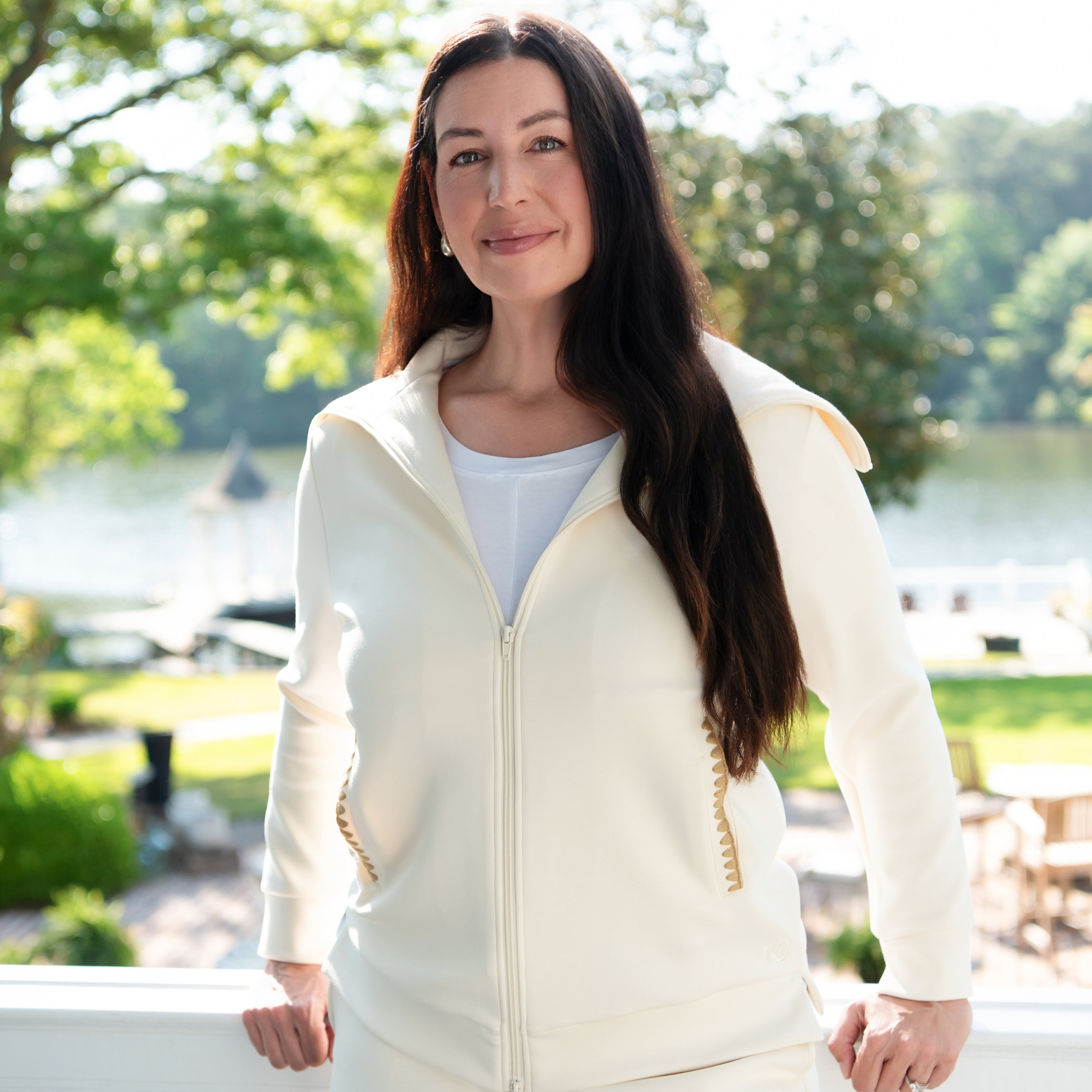 Woman wearing a cream-colored loungewear set outdoors with trees and water in the background