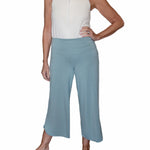 Woman wearing sage green pants highlighting the adaptive adjustable waistband that folds over against a white background