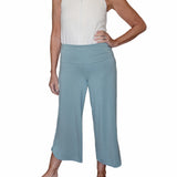 Woman wearing sage green pants highlighting the adaptive adjustable waistband that folds over against a white background