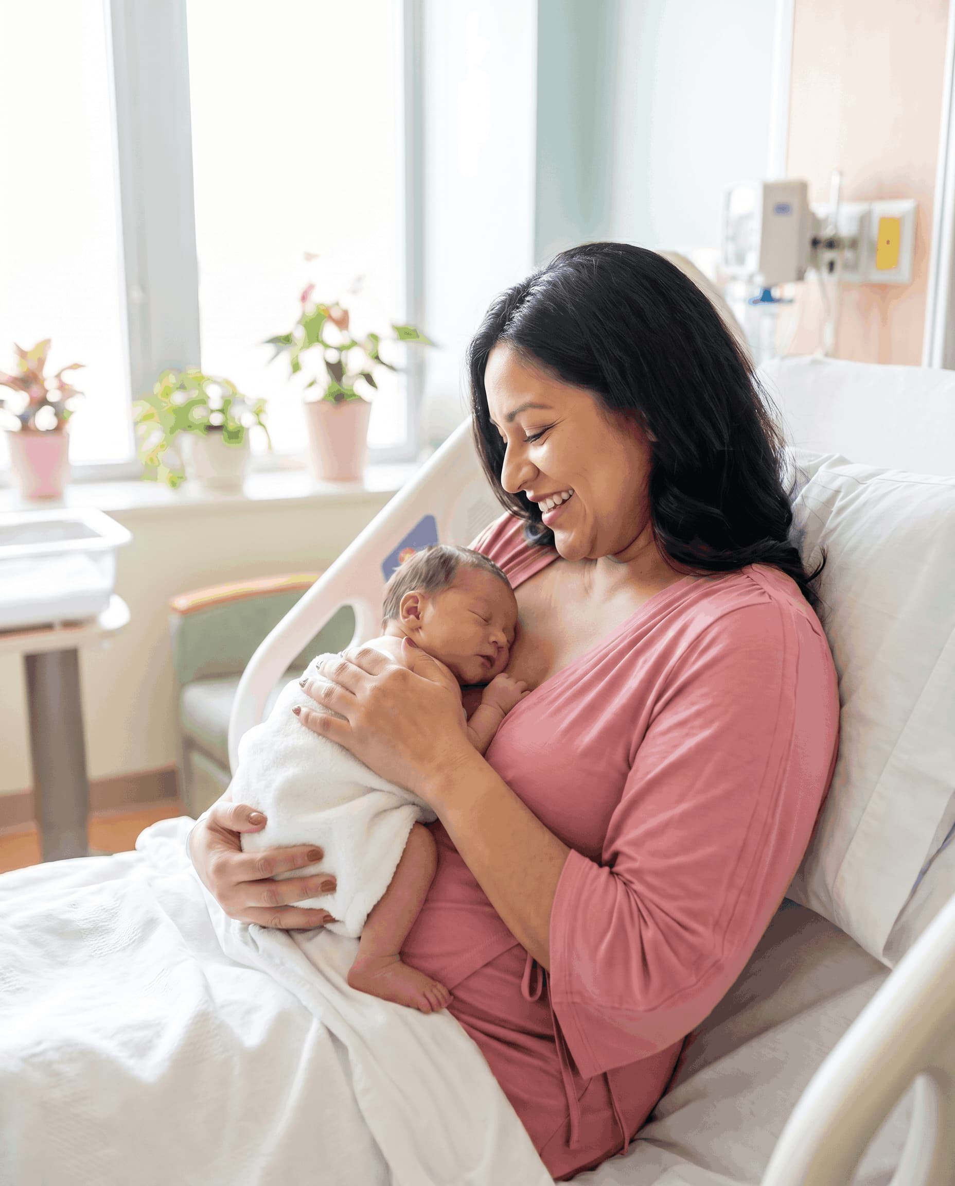 Woman in a hospital bed holding a newborn baby doing skin to skin postpartum