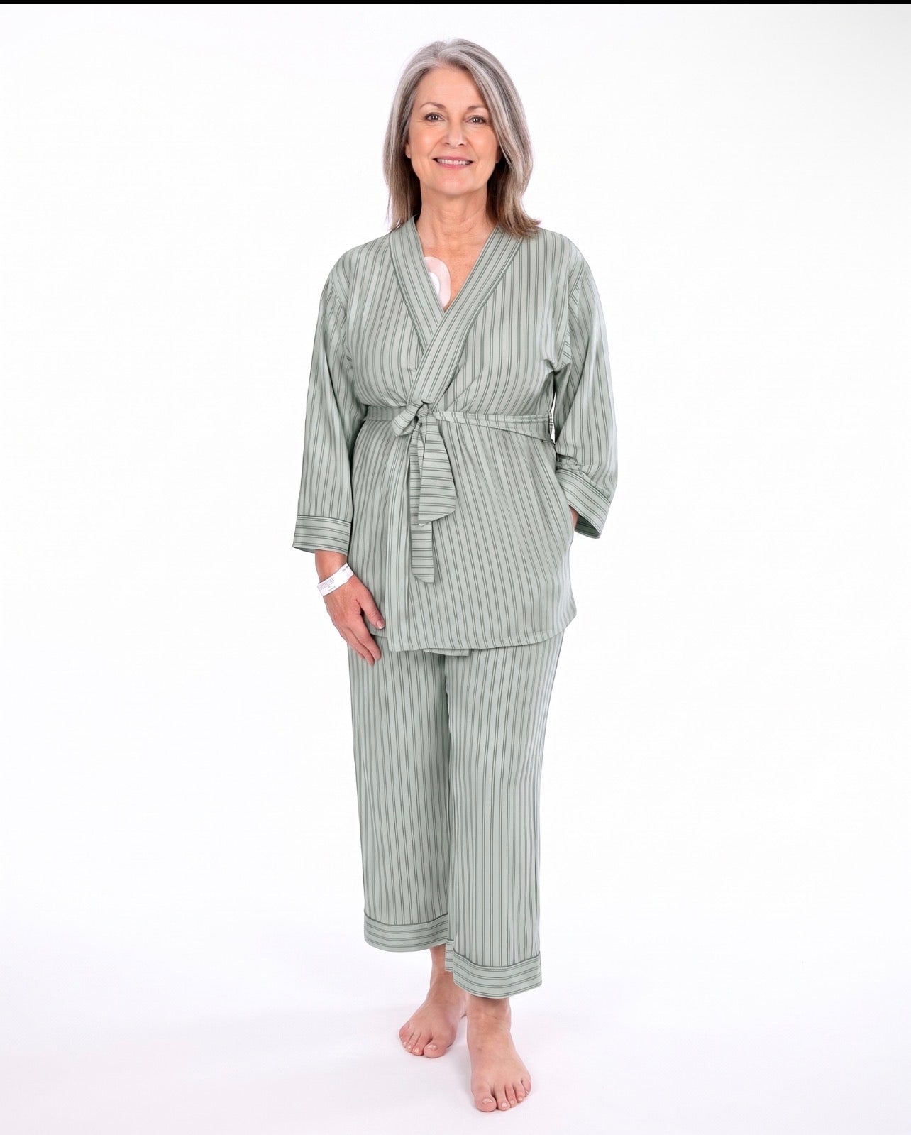 A woman modeling a two-piece sage green pajama set with vertical stripes, consisting of a long-sleeve tie-front robe and matching pants, against a plain white background.