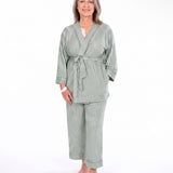 A woman modeling a two-piece sage green pajama set with vertical stripes, consisting of a long-sleeve tie-front robe and matching pants, against a plain white background.