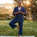 Woman practicing yoga outdoors in a natural setting with trees and sunlight in the navy kickit pajamas set