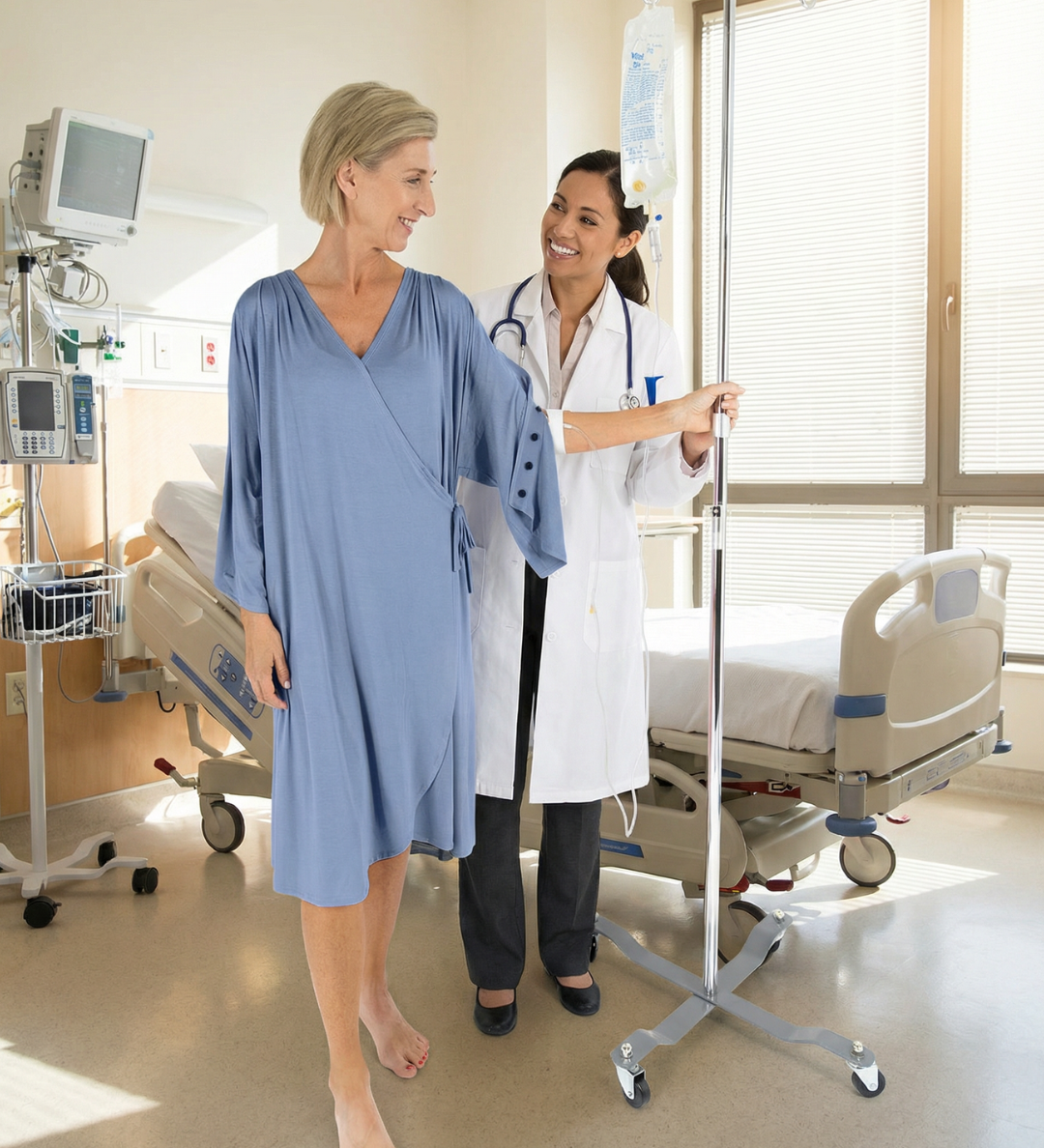 Woman in a hospital gown walking with a doctor in a hospital room.