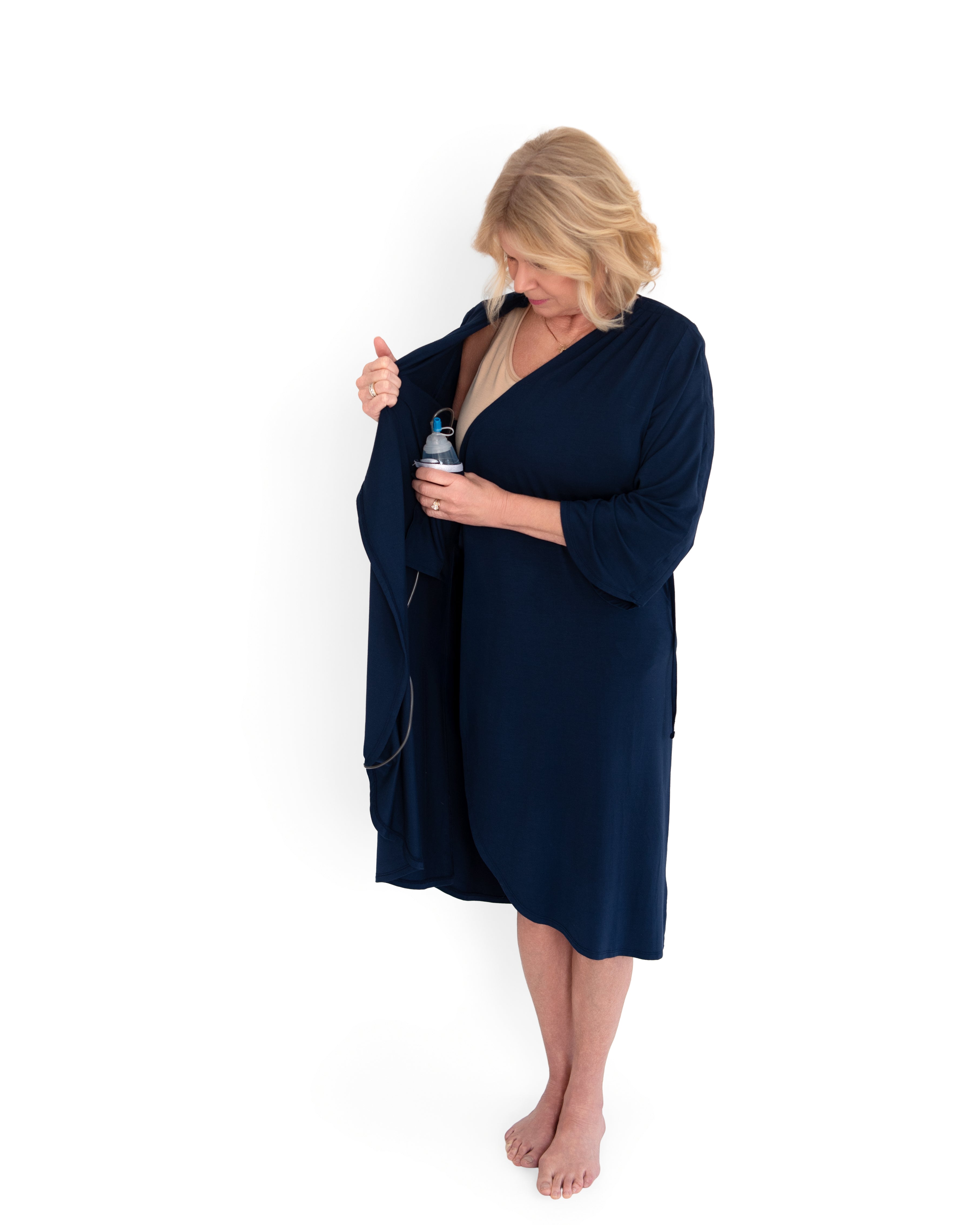 Woman wearing a navy blue hospital gown holding a surgical bulb inserting it in to the inside pocket of the robe on a white background