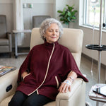 Woman wearing a maroon infusion jacket while attached to an IV pole in a treatment room