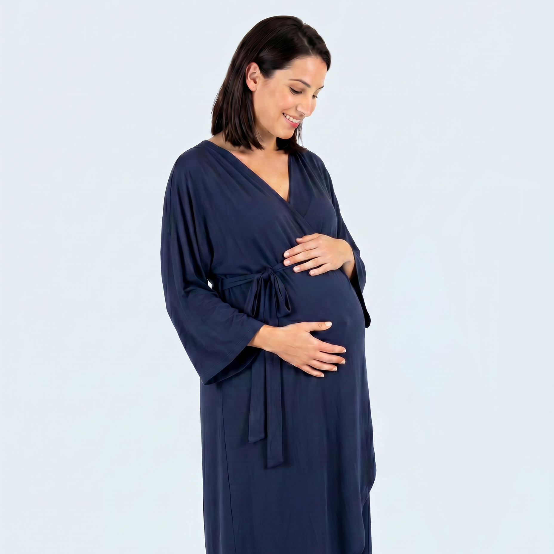 A pregnant woman wearing a navy blue hospital gown with three-quarter sleeves and a tie waist, standing against a light gray studio background.