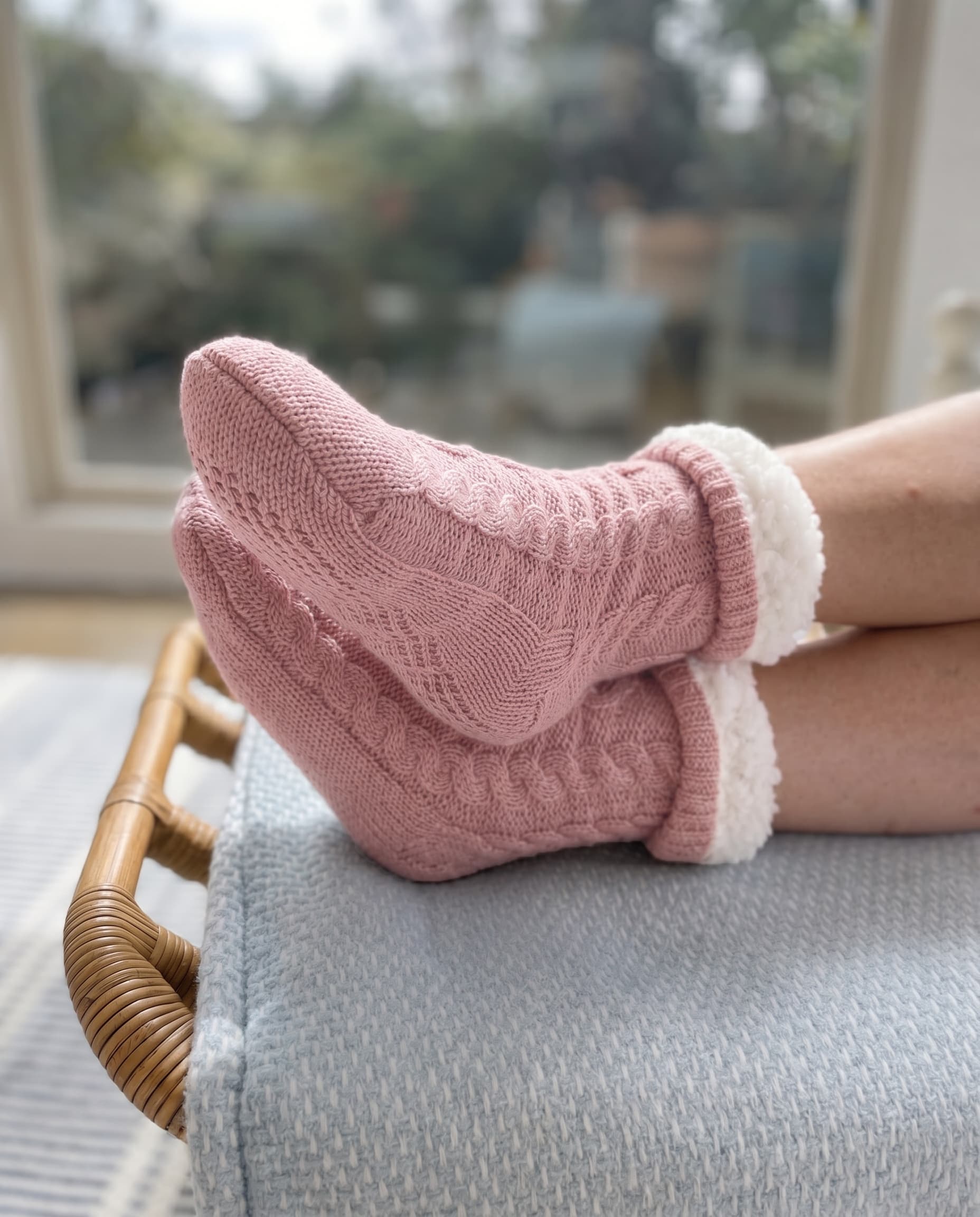 Person wearing pink cable knit socks with white fleece interior cuffed at the top on a light blue cushion.