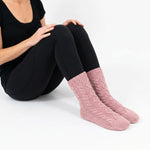 Person wearing pink cable knit socks on a white background