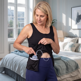 woman wearing a black mastectomy tank top showing the interior drain pockets against a bedroom background