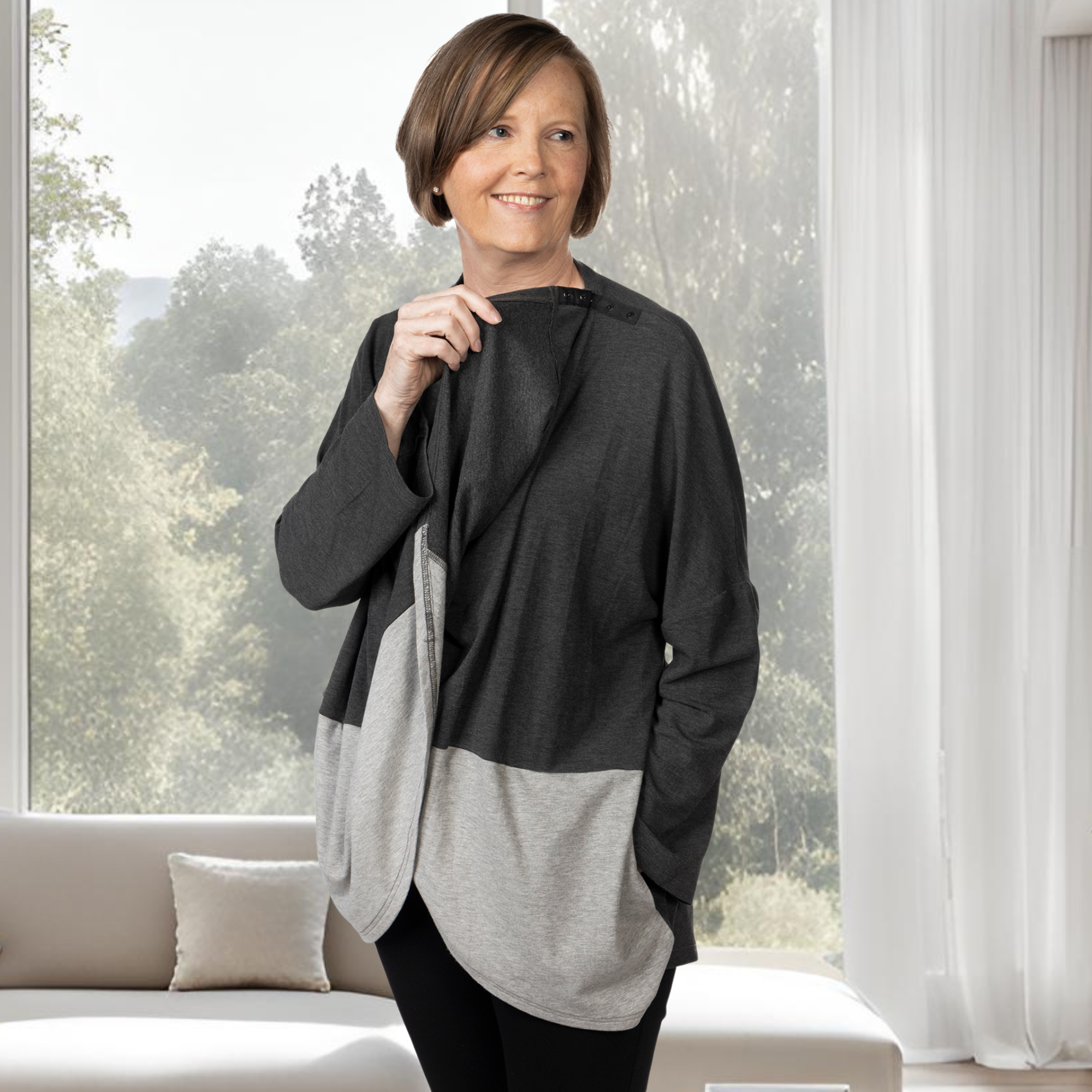 Woman wearing a gray color-blocked shirt with snap neck closure in a bright room with large windows.