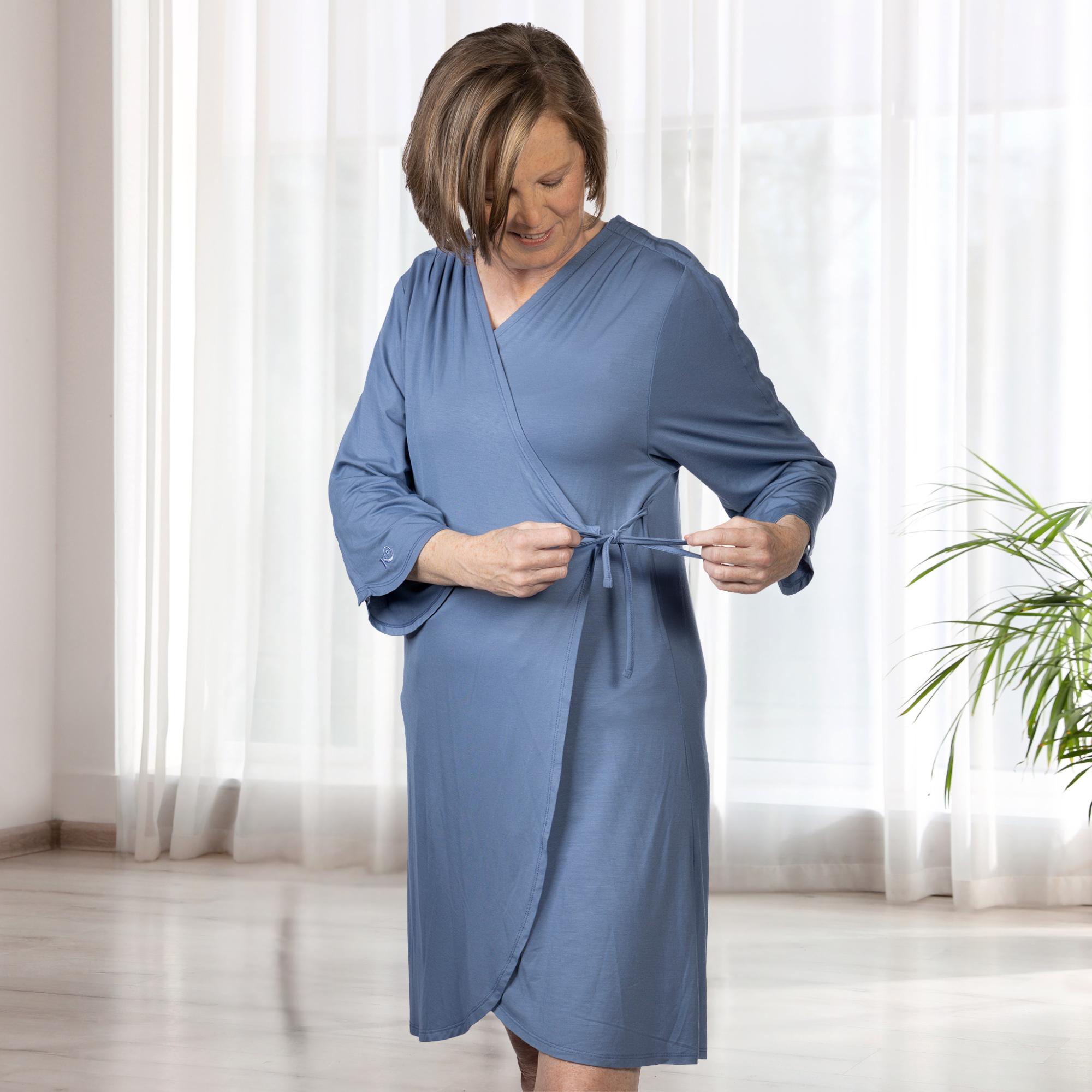 Woman wearing a blue robe in a bright room with white curtains.